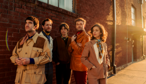 Members of punch brothers stsanding in front of brick building during sunset.