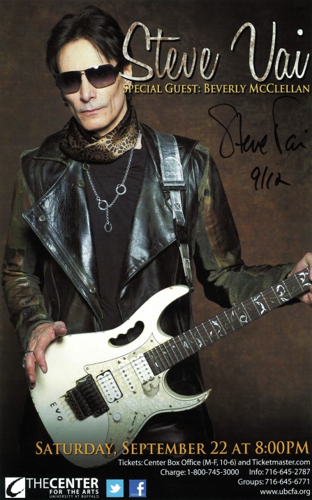 steve vai wearing sunglasses posing with an electric guitar.