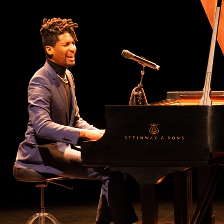 jon batiste performing on the piano while singing.