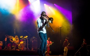 A trumpeter performs on stage with colored lights in the background. 