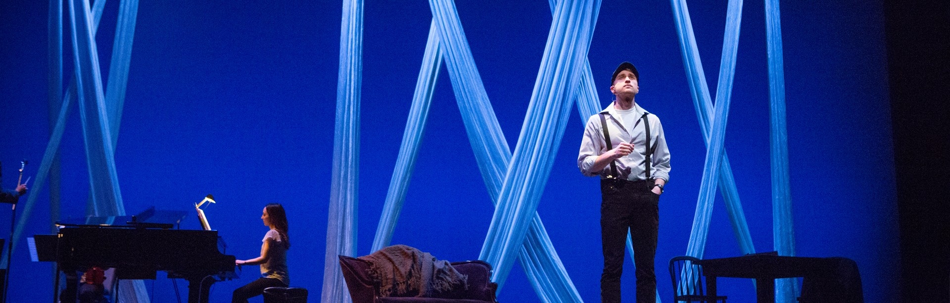 A student performs on stage with a piano player in the background.
