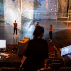 Stage with rehearsal and students working at control and sound board computers from up in the seating. 