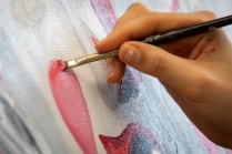 Close up of a hand holding a paint brush to a canvas. 
