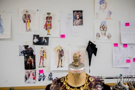 A dress form in the foreground, with designs pinned to wall in background. 
