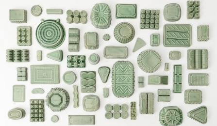 A birds eye photograph of many ceramic objects, all the same shape as plastic containers and glazed in green. 