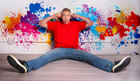 gary owen sitting against a wall with paint splatters with legs spread out. 