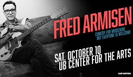 fred armisen sitting on a couch holding a guitar. 