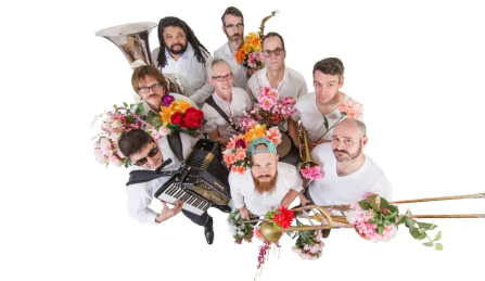 Members of Slavic Soul Party standing in a group close together holding their instruments and looking up. 