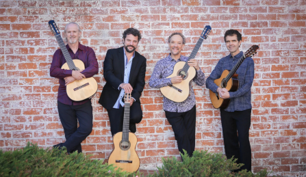 Members of LA Guitar Quartet standing in front of a brick wall holding their acoustic guitars. 