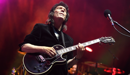 Steve Hackett playing guitar on stage with eyes closed head raised. 