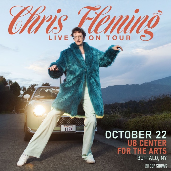 chris fleming posing in front of a car wearing a faux fur coat with mountains and trees in the background. 