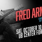 fred armisen sitting on a couch holding an electric guitar. 