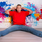 gary owen sitting against a wall with paint splatters with legs spread out. 