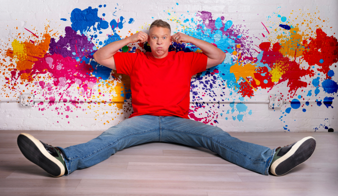 gary owen sitting against a wall with paint splatters with legs spread out. 