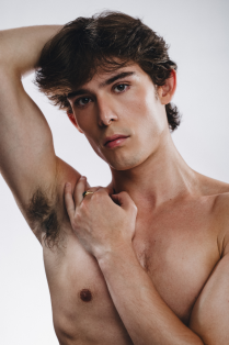 drazen wilmers posing without a shirt on with one hand on shoulder and the other above his head. 