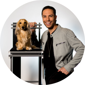 alex ramon kneeling next to small dog sitting on a chair. 